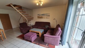 A living room with a staircase, a sofa set, a coffee table, and a window with a view. - Ferienhaus in Nessmersiel (Dornum)