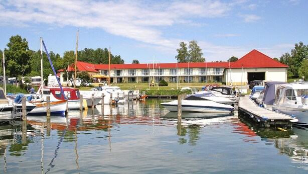 A marina with boats docked in front of a building with a red roof. - Aparthotel by Lake Heidensee With Boat Rentals (Schwerin)