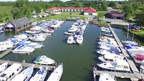A marina with multiple boats docked, a large building with a red roof, and a smaller structure to the left. - Aparthotel by Lake Heidensee With Boat Rentals (Schwerin)