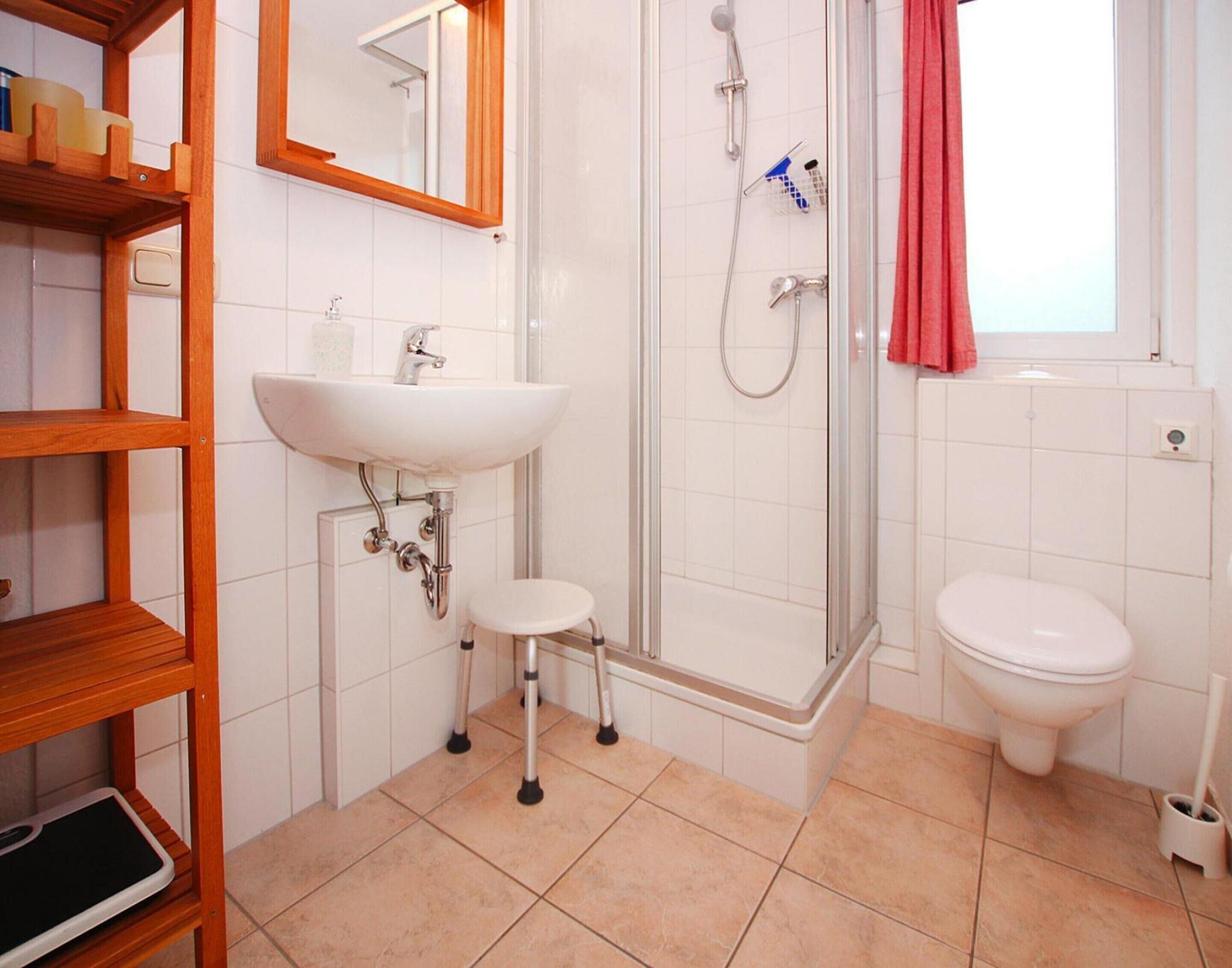 Une salle de bain avec un lavabo blanc, des toilettes, une douche avec une porte en verre et une étagère en bois.
