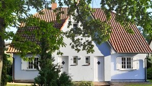 Ein weißes Haus mit rotem Ziegeldach, einem Ziegelweg und einem kleinen Baum im Vordergrund.
