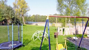 A playground with a swing set, a trampoline, and a climbing structure in a grassy yard with trees and a fence in the background. - Ferienwohnung Alte Schmiede, Zemitz (Zemitz)