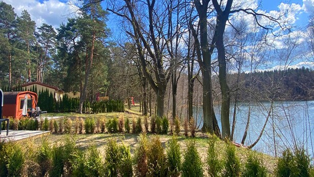 Una proprietà sul lago con un molo di legno, un piccolo edificio rosso e un giardino curato con siepi potate.