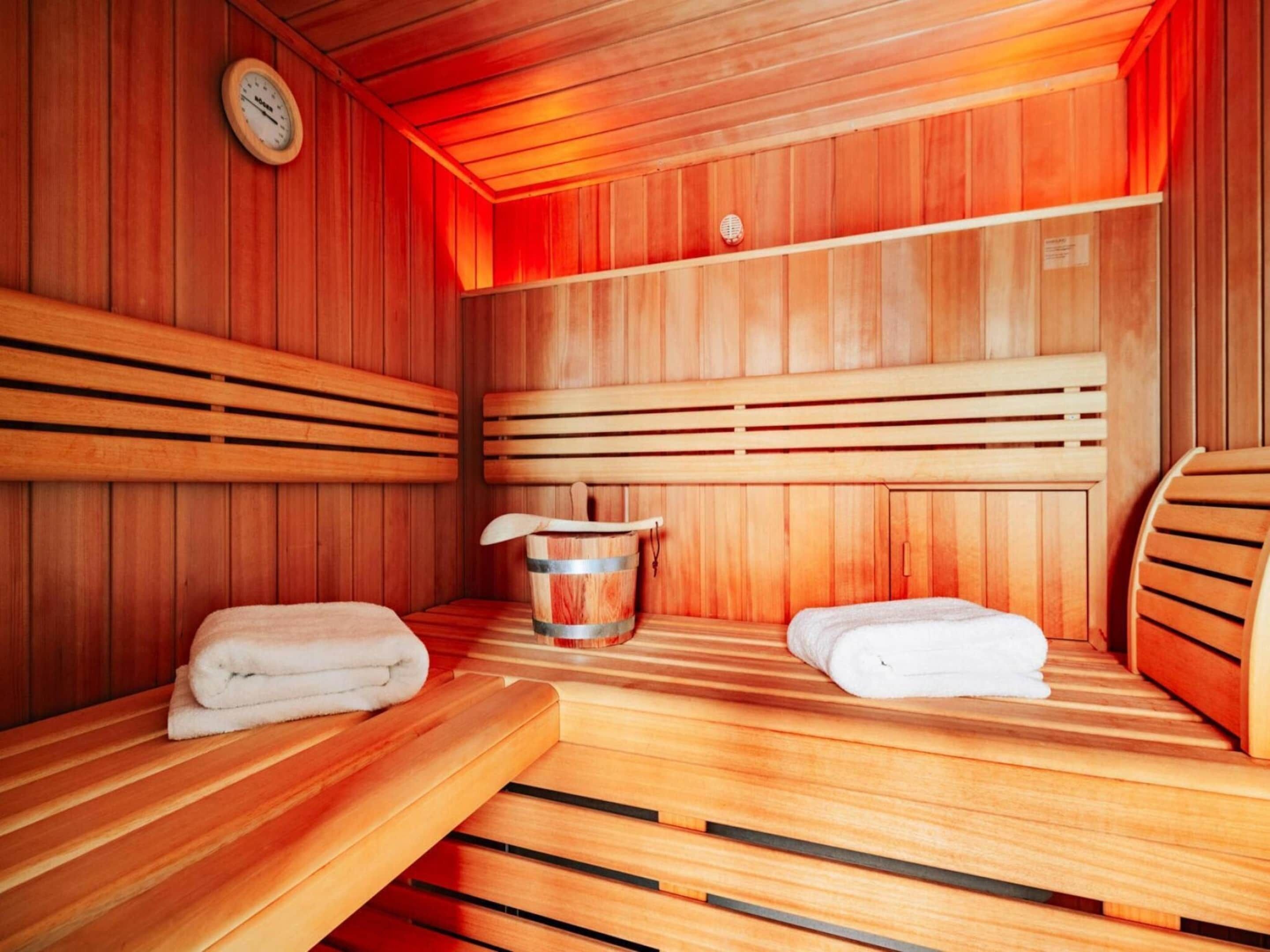A sauna room with wooden benches, a bucket, and towels.