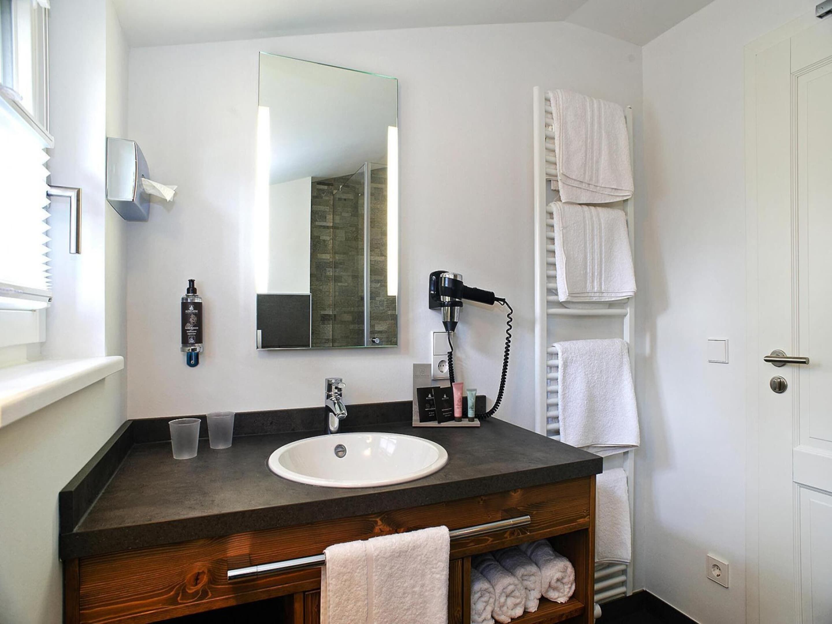 A bathroom with a white sink, a mirror, a hairdryer, and a towel rack.