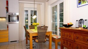 Een compacte keuken met een eettafel, stoelen, een koelkast, een oven en een koffiezetapparaat.