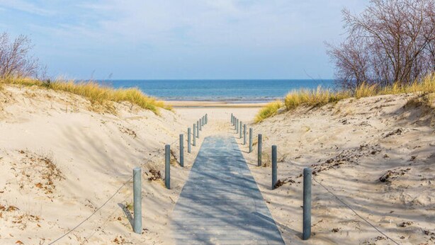 Een zandpad dat naar een strand leidt, onder een heldere lucht.