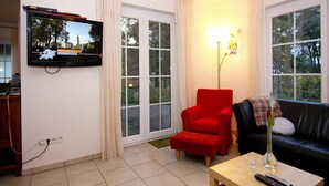 Een woonkamer met een televisie, een rode fauteuil, een zwarte bank en een salontafel met afstandsbedieningen.
