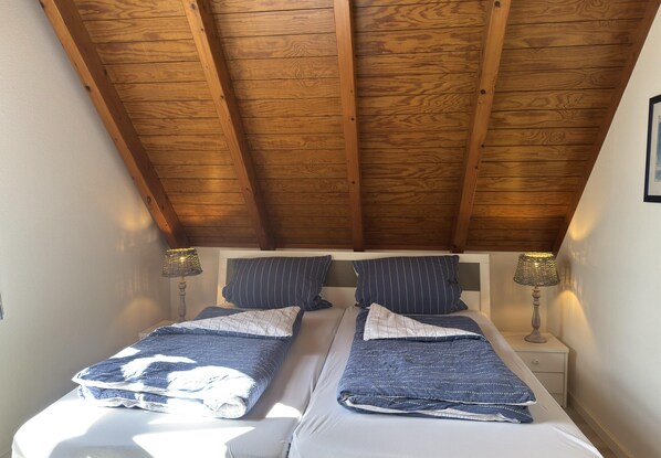 A bedroom with two beds, wooden ceiling beams, bedside lamps, and a framed picture on the wall. - Ferienhaus Fischer Sien Huus, Steinhude (Wunstorf)