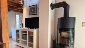 Ein Wohnzimmer mit Fernseher, weißem Unterhaltungsschrank und einem schwarzen Holzofen.