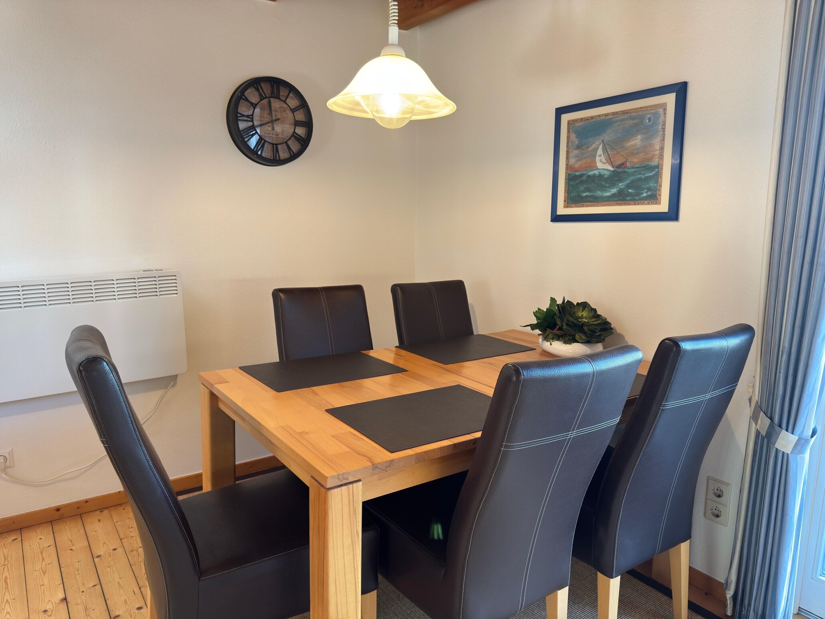 A dining area with a wooden table, black leather chairs, a clock, a pendant light, and a framed painting.
