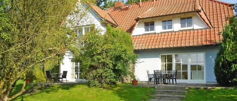 A two-story house with a red-tiled roof, large windows, and a well-maintained lawn.