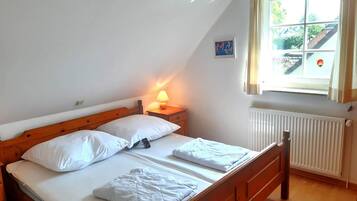 Uma cama de solteiro com lençóis brancos, cabeceira de madeira, mesa de cabeceira com abajur e janela com cortinas.