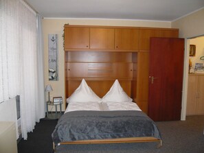 A bedroom with a bed, a wooden wardrobe, a door, and a small table with a lamp. - Apartment, Cuxhaven (Cuxhaven)