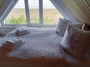 Un dormitorio con un ventanal grande, una cama con una manta texturizada y almohadas con forma de estrella de mar.
