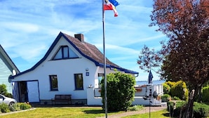 Une maison blanche avec un toit bleu, un mât sur lequel flotte un drapeau, un banc et un petit bateau.