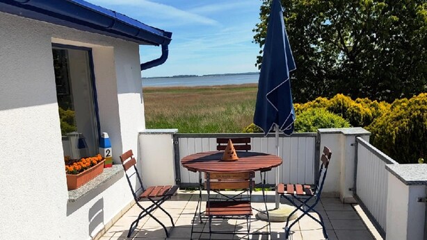 Une terrasse avec une table et des chaises, un parasol bleu et une vue sur la mer.