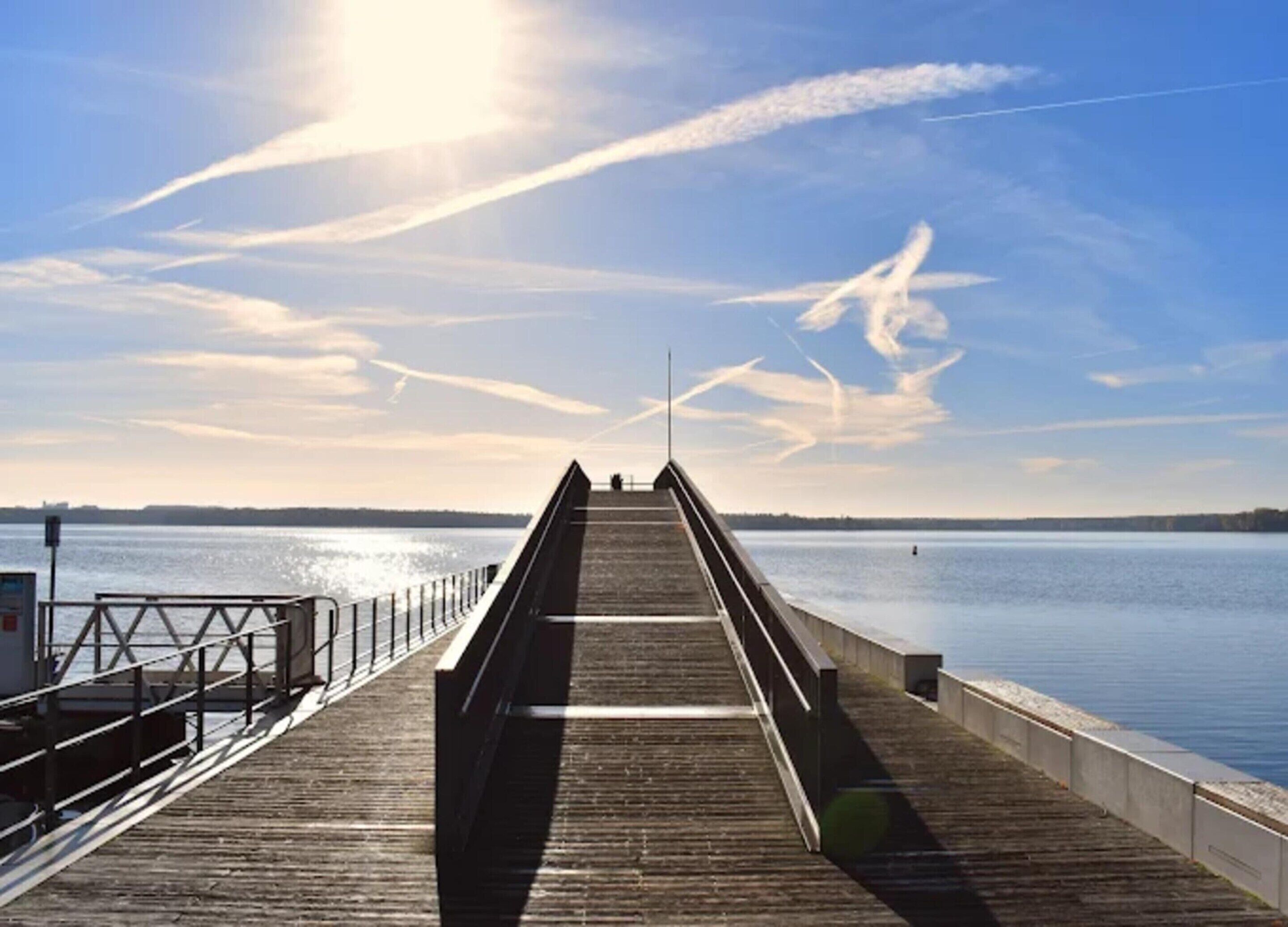 Une jetée en bois s’étendant sur une étendue d’eau calme, sous un ciel dégagé.