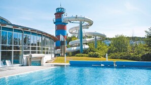A swimming pool with a water slide, a tall tower, and a building with large windows. - Ferienwohnungen im Seepark Sellin (Sellin)
