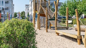 A wooden play structure with a rope bridge and climbing net, set on sandy ground with a bench nearby. - Ferienwohnungen im Seepark Sellin (Sellin)
