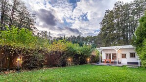 A modern house with a covered patio, surrounded by a lush garden and tall trees. - Ferienhaus am Wockersee in Parchim (Parchim)