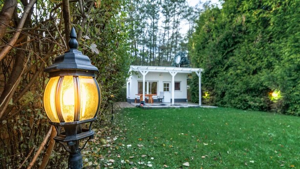 A garden with a lamp post and a white building with a porch. - Ferienhaus am Wockersee in Parchim (Parchim)