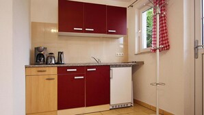 A compact kitchen with red and white cabinets, a coffee maker, and a dishwasher. - Ferienhaus am Wockersee in Parchim (Parchim)