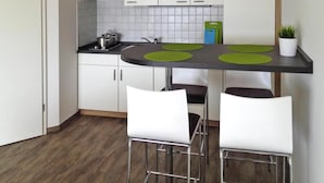 A modern kitchen with white cabinets, a black countertop, and green placemats. There are two white bar stools and a potted plant on the countertop. - Appartements am Heidensee in Schwerin (Schwerin)