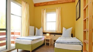 A room with two beds, a wooden floor, a window with curtains, and a small table with a lamp. - Apartment in Plau am See mit Terrasse (Plau am See)