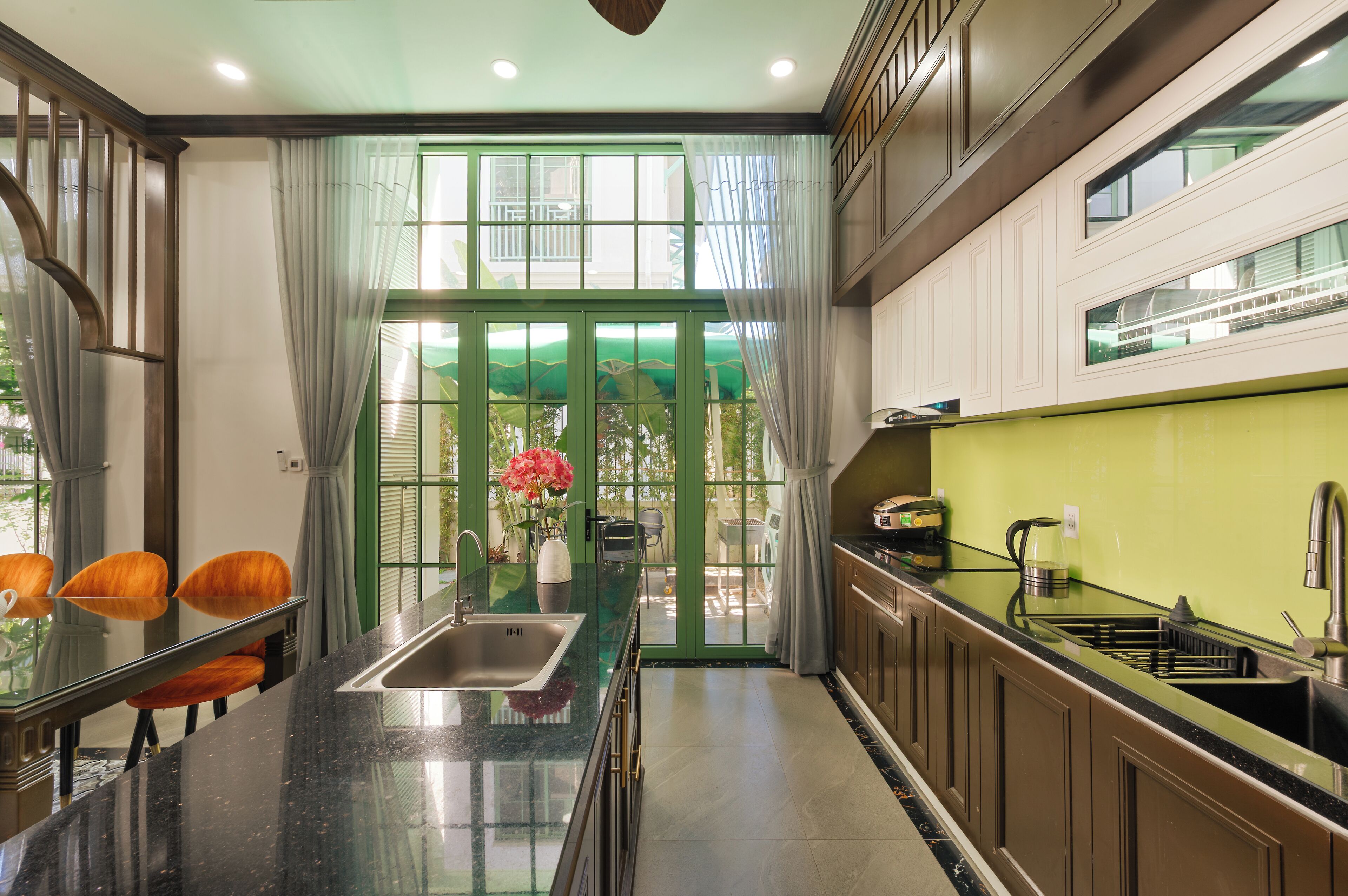 A modern kitchen with a central island, a sink, and a dining area with chairs.