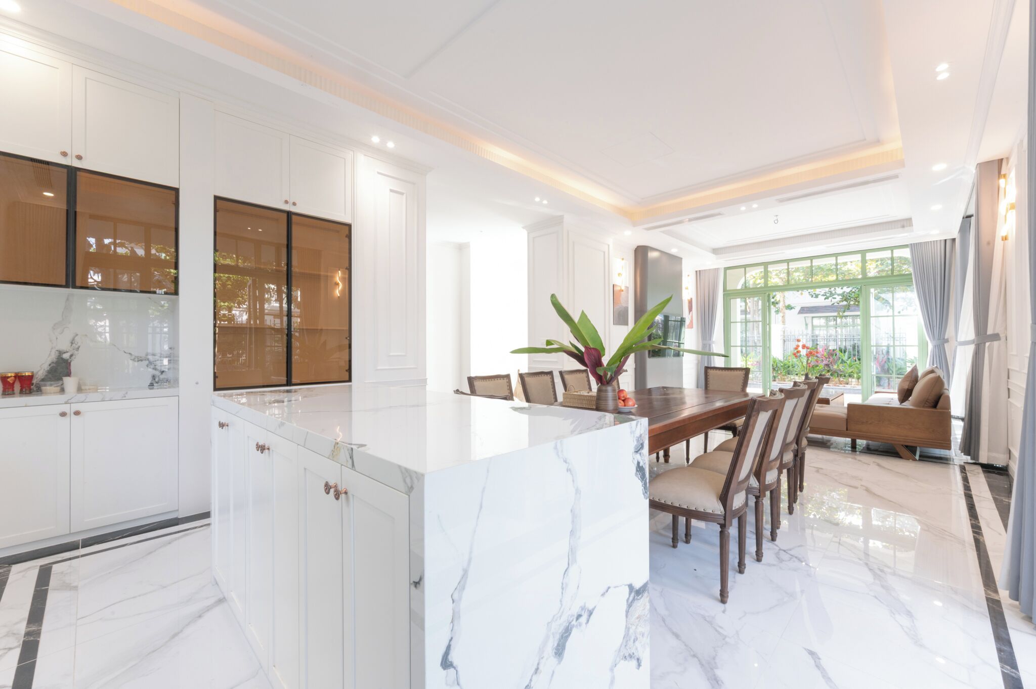 Una cocina moderna con armarios blancos, una isla de mármol y un comedor con mesa y sillas de madera.