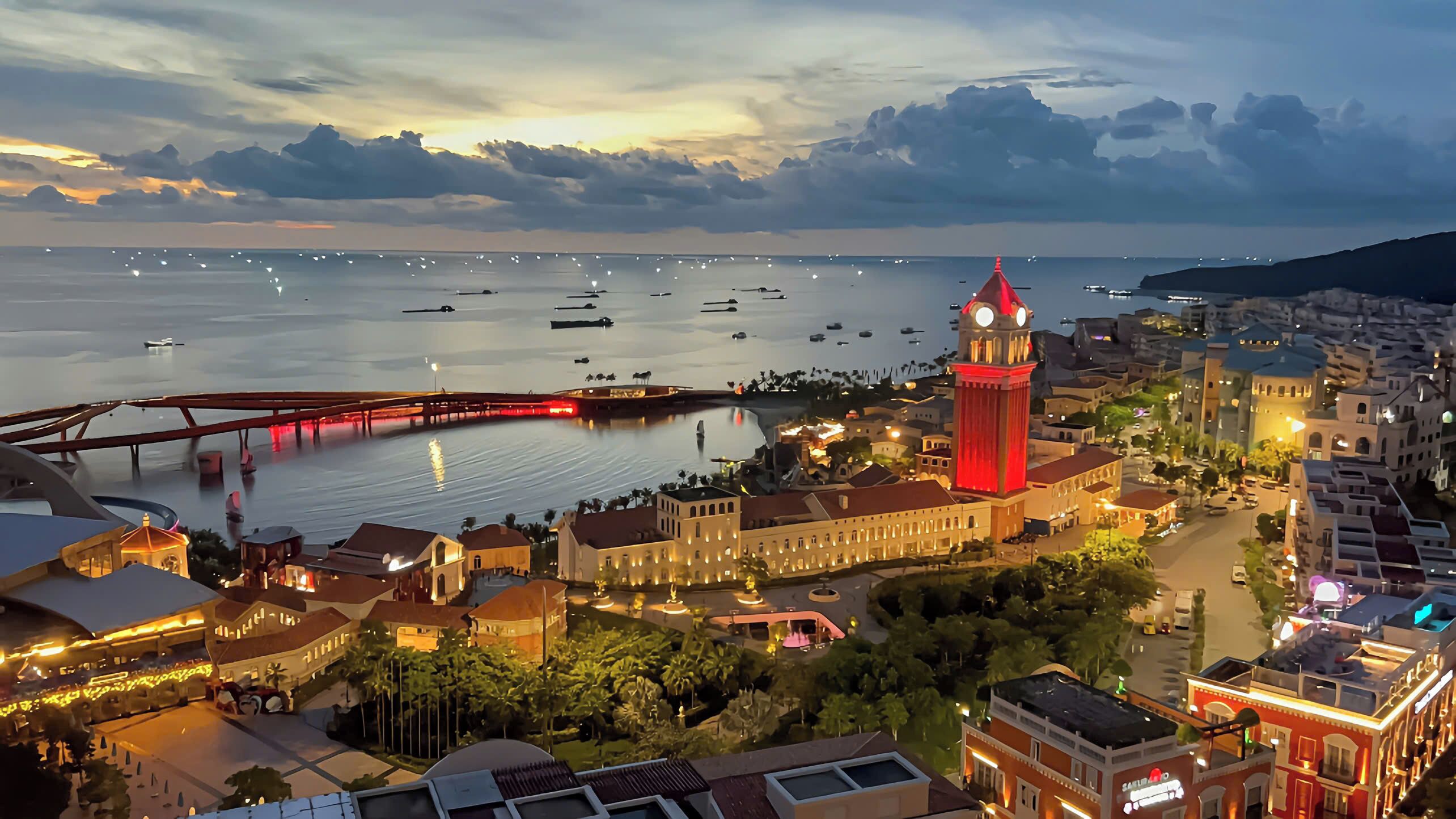 Un paisaje urbano costero con una imponente torre del reloj, un puente y una marina llena de barcos.