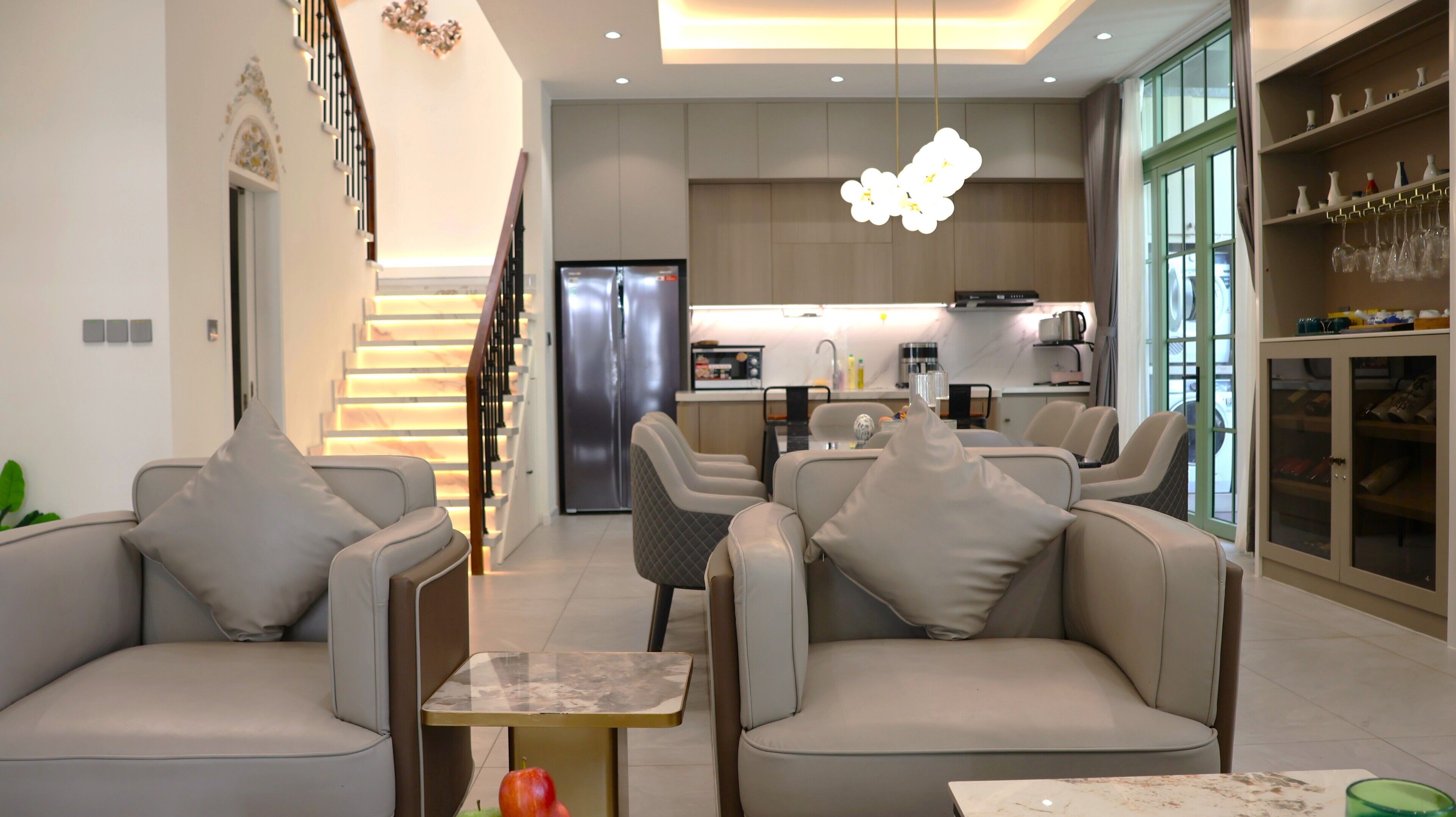A modern living room with a sofa set, a dining table, and a kitchen in the background.