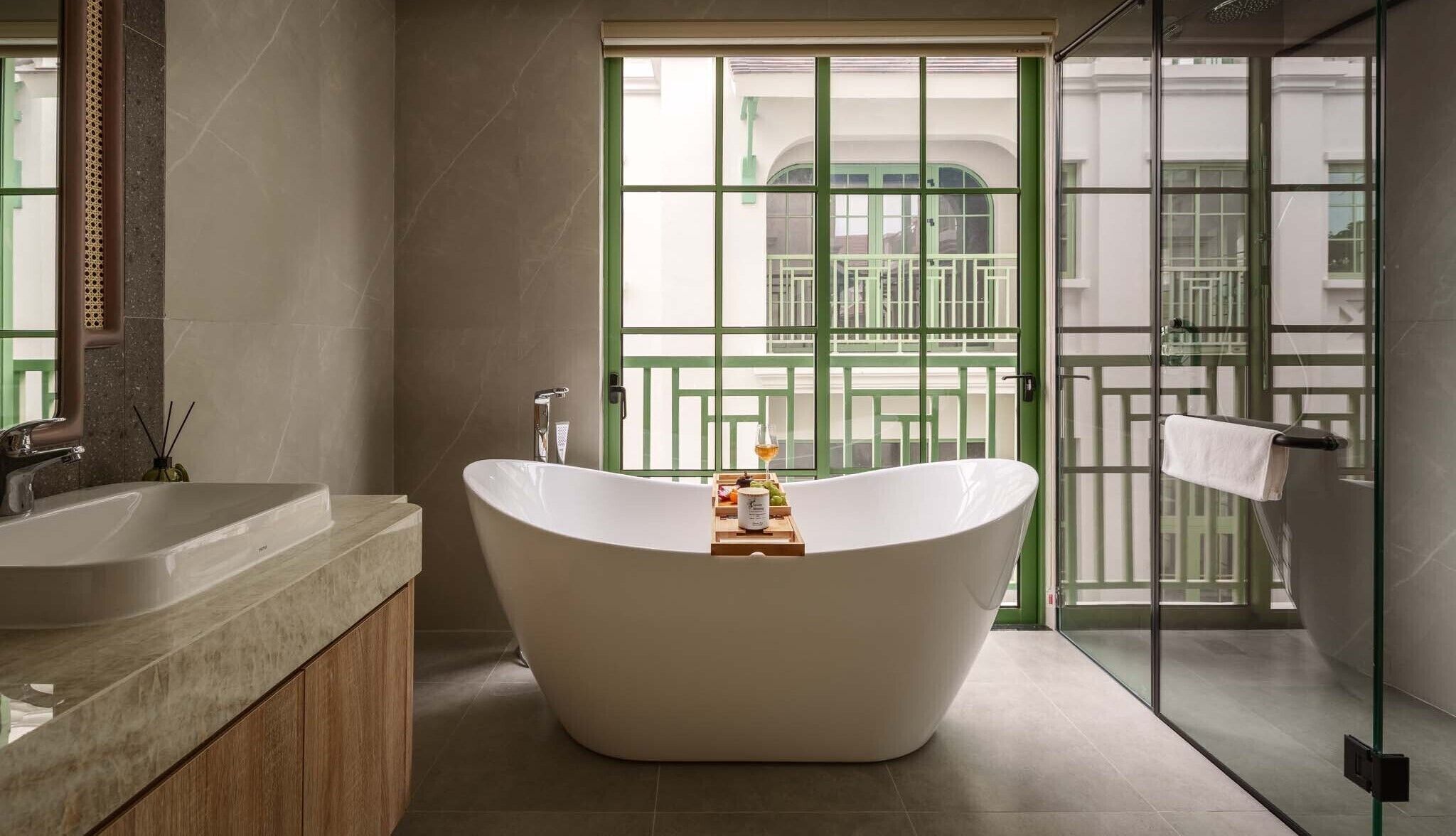 A modern bathroom with a freestanding bathtub, a large mirror, and a view of a green balcony.