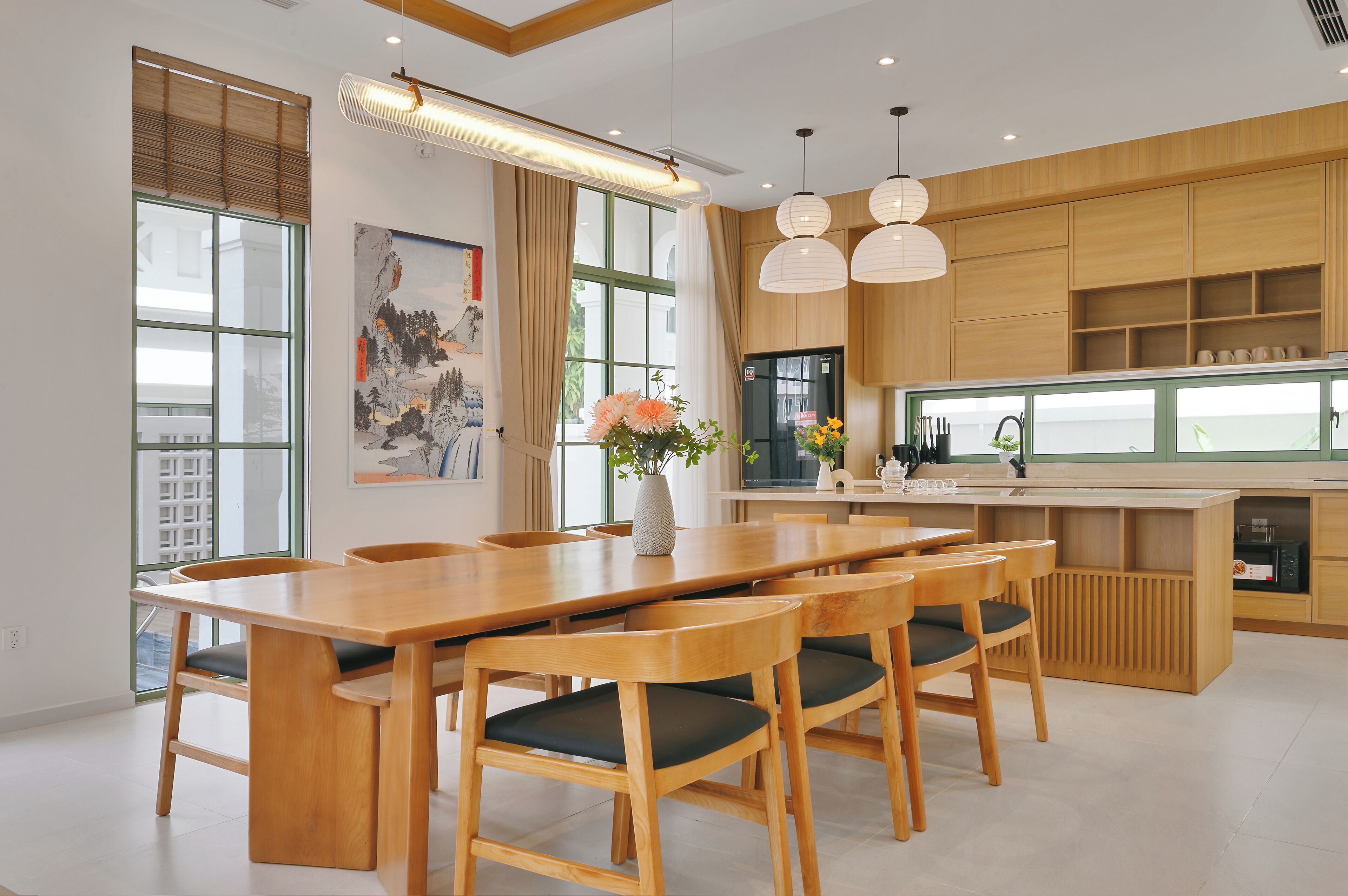 Una cucina moderna con mobili in legno, una zona pranzo con un tavolo lungo e sedie, e lampade a sospensione.