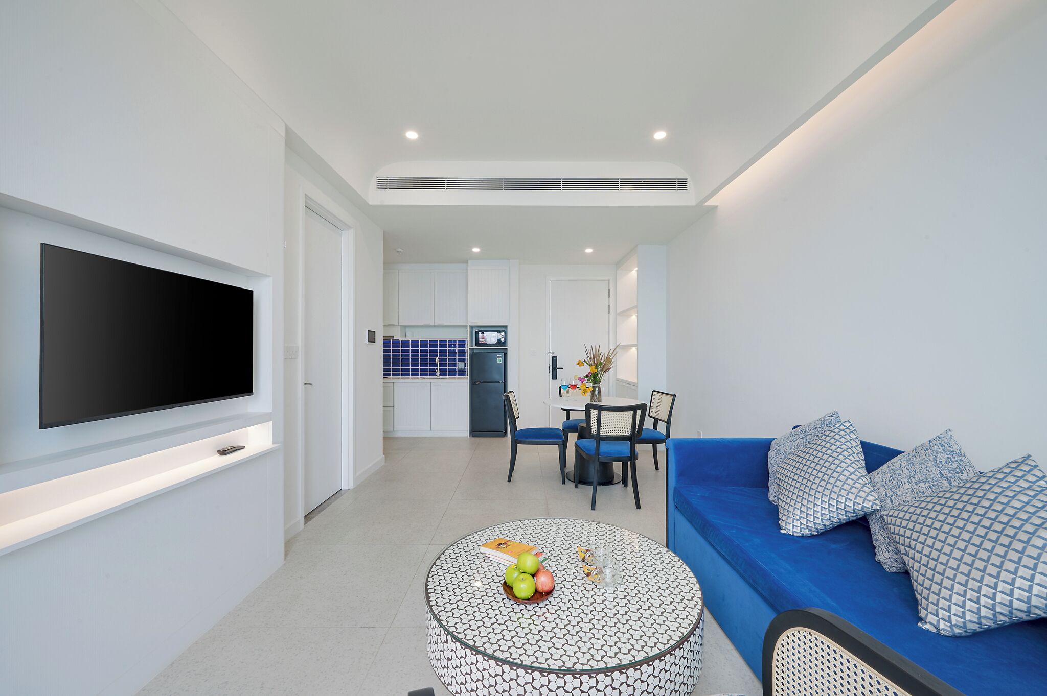 Un salon moderne doté d’un téléviseur à écran plat, d’un canapé bleu et d’un coin repas avec une table et des chaises.