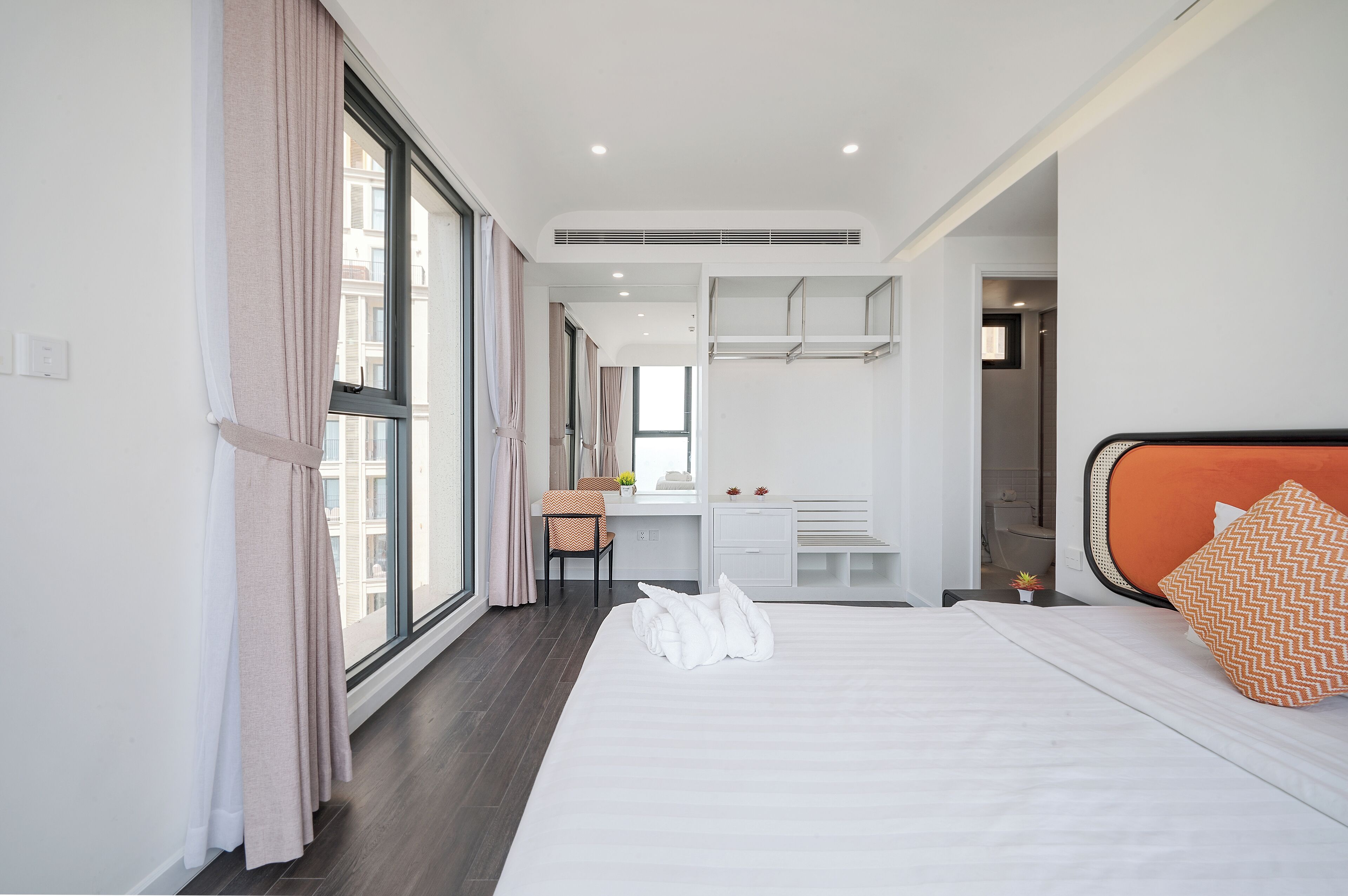 A modern hotel room with a large bed, a desk, and a bathroom visible through an open door.