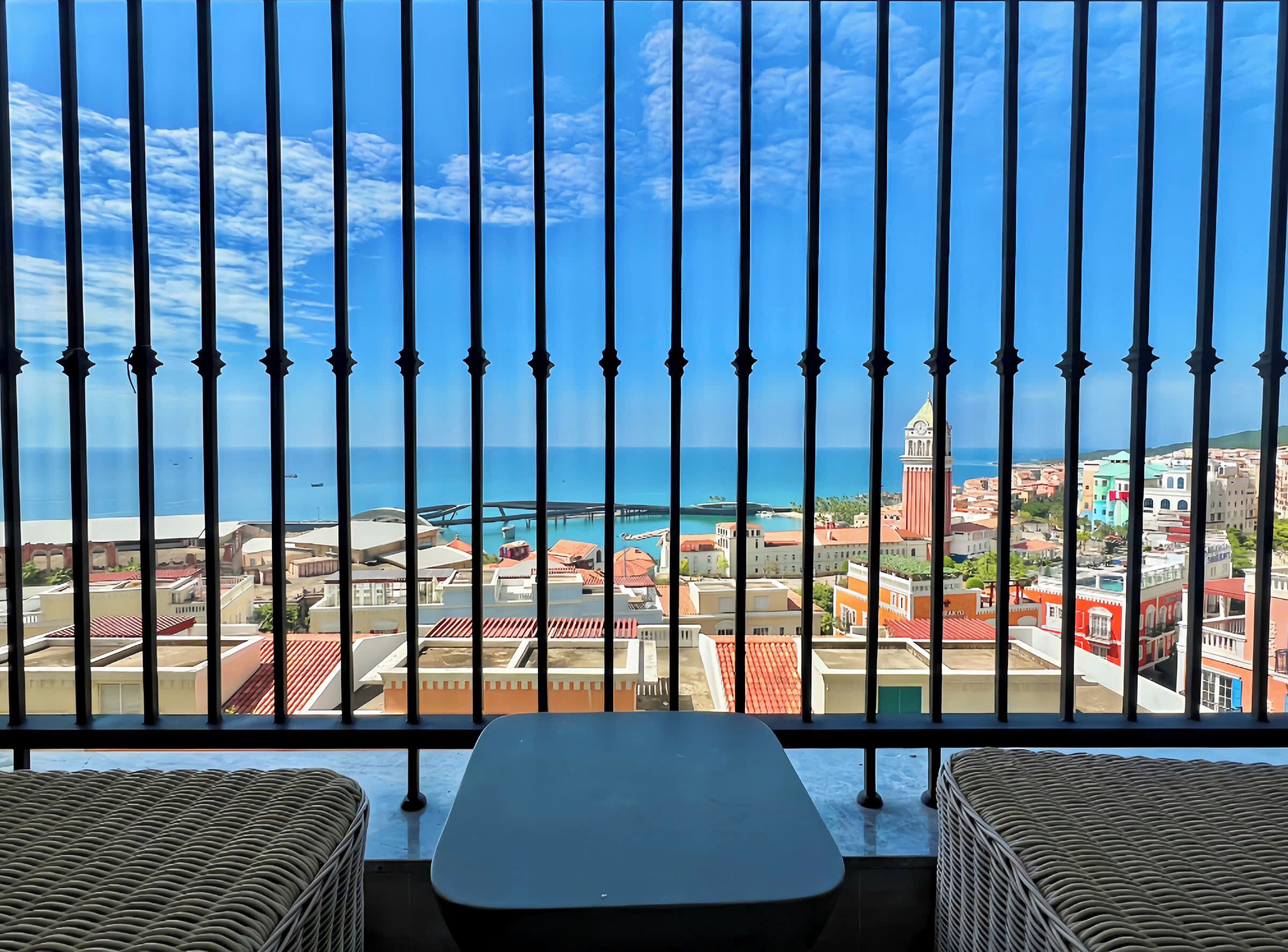 Un balcón con vistas a un pueblo costero, que incluye edificios, una torre y el mar.