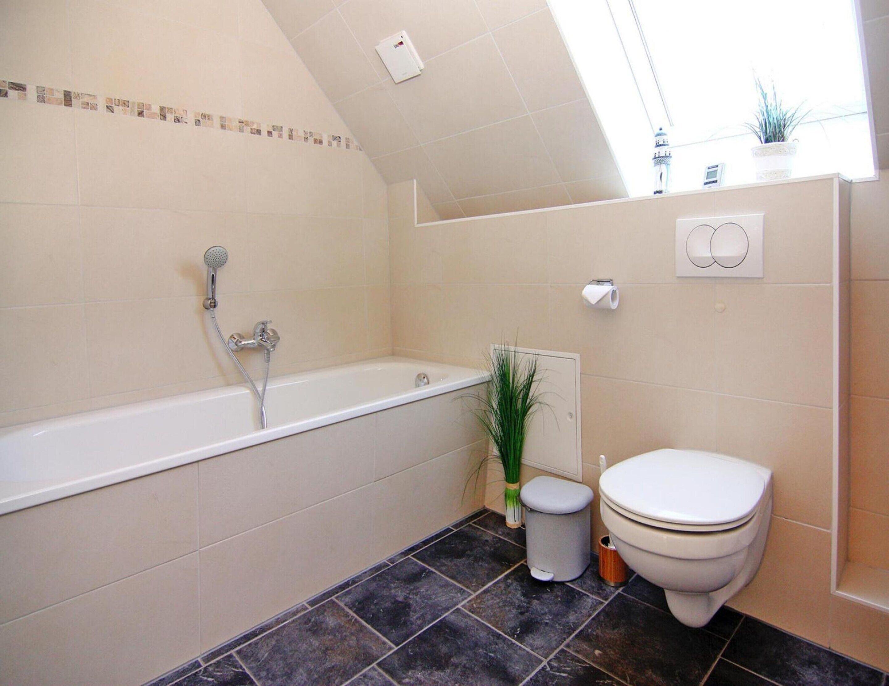 A bathroom with a bathtub, toilet, and a small trash bin.