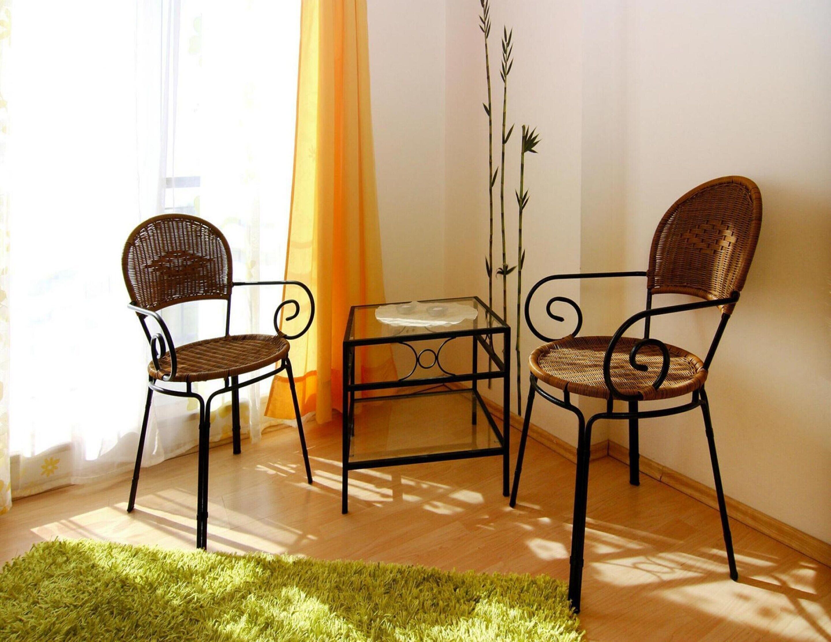 A room with two wicker chairs, a glass table, and a green rug.