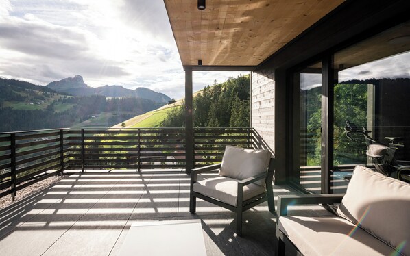 A balcony with a view of a mountainous landscape, a cushioned chair, and a sofa. - Aois 4 Elements suits (La Valle)