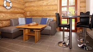 A log cabin interior with a wooden dining table, two bar stools, a sofa with blue cushions, and a wooden bench. - Blockhaus in Trassenheide (Trassenheide)