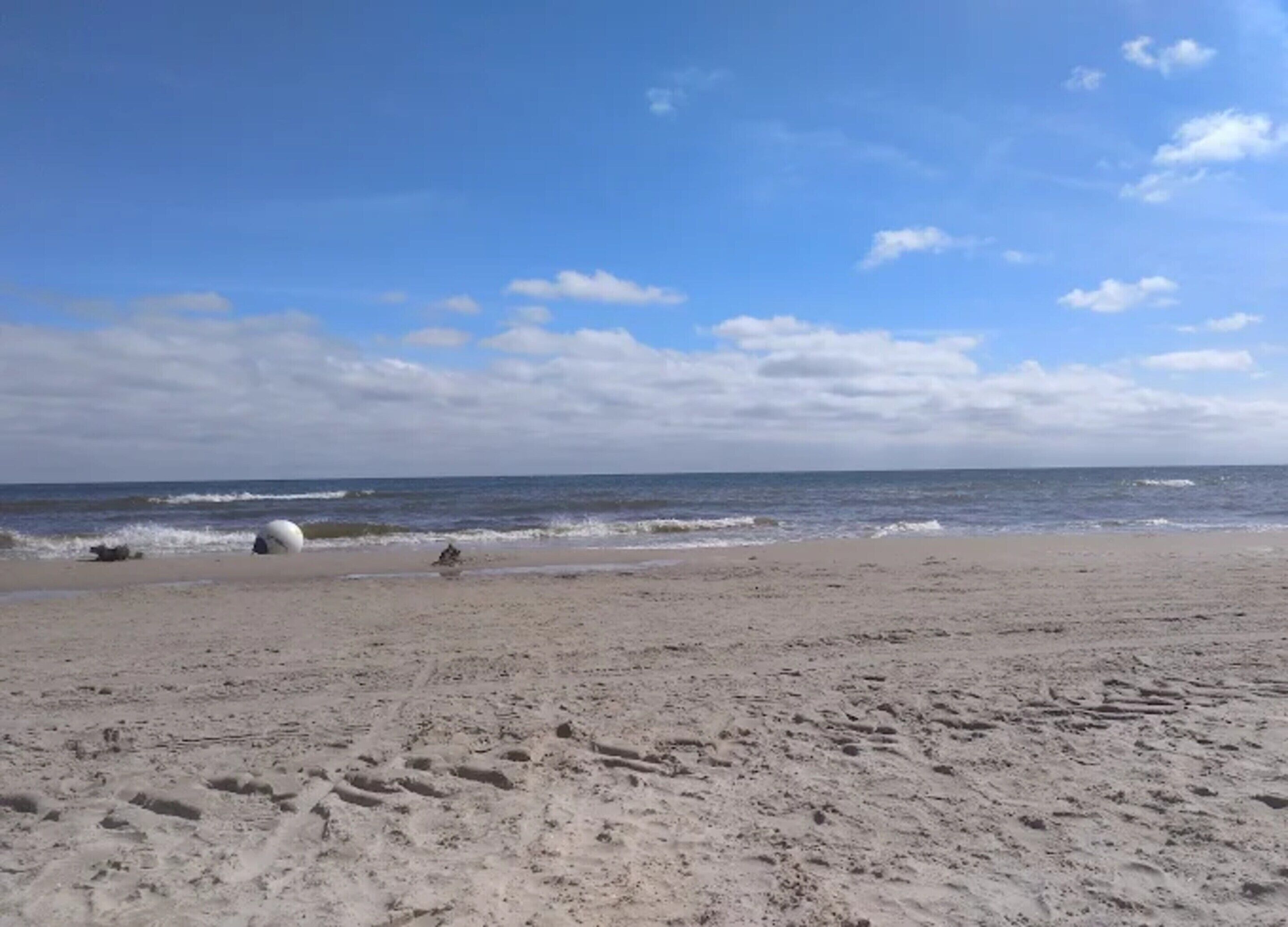 A sandy beach with footprints and a large white object, likely a ball, in the distance.