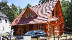 A log cabin with a red-tiled roof, a car parked in front, and a fenced area with a statue. - Blockhaus in Trassenheide (Trassenheide)