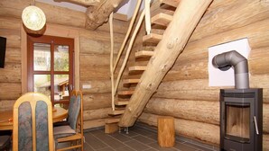 A log cabin interior with a wooden staircase, a dining table with chairs, and a wood-burning stove. - Blockhaus in Trassenheide (Trassenheide)