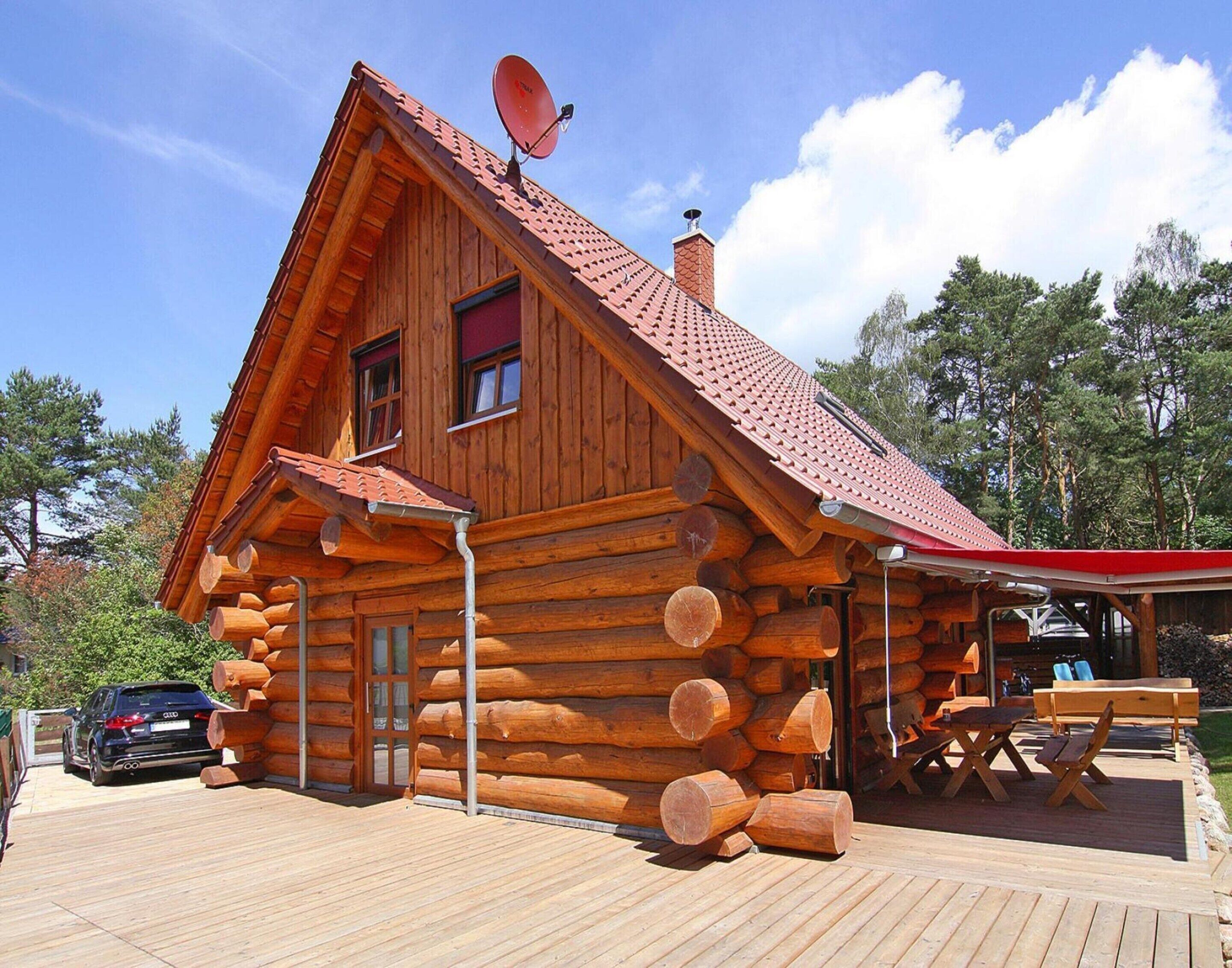 A log cabin with a red roof, a satellite dish, and a deck with outdoor seating.