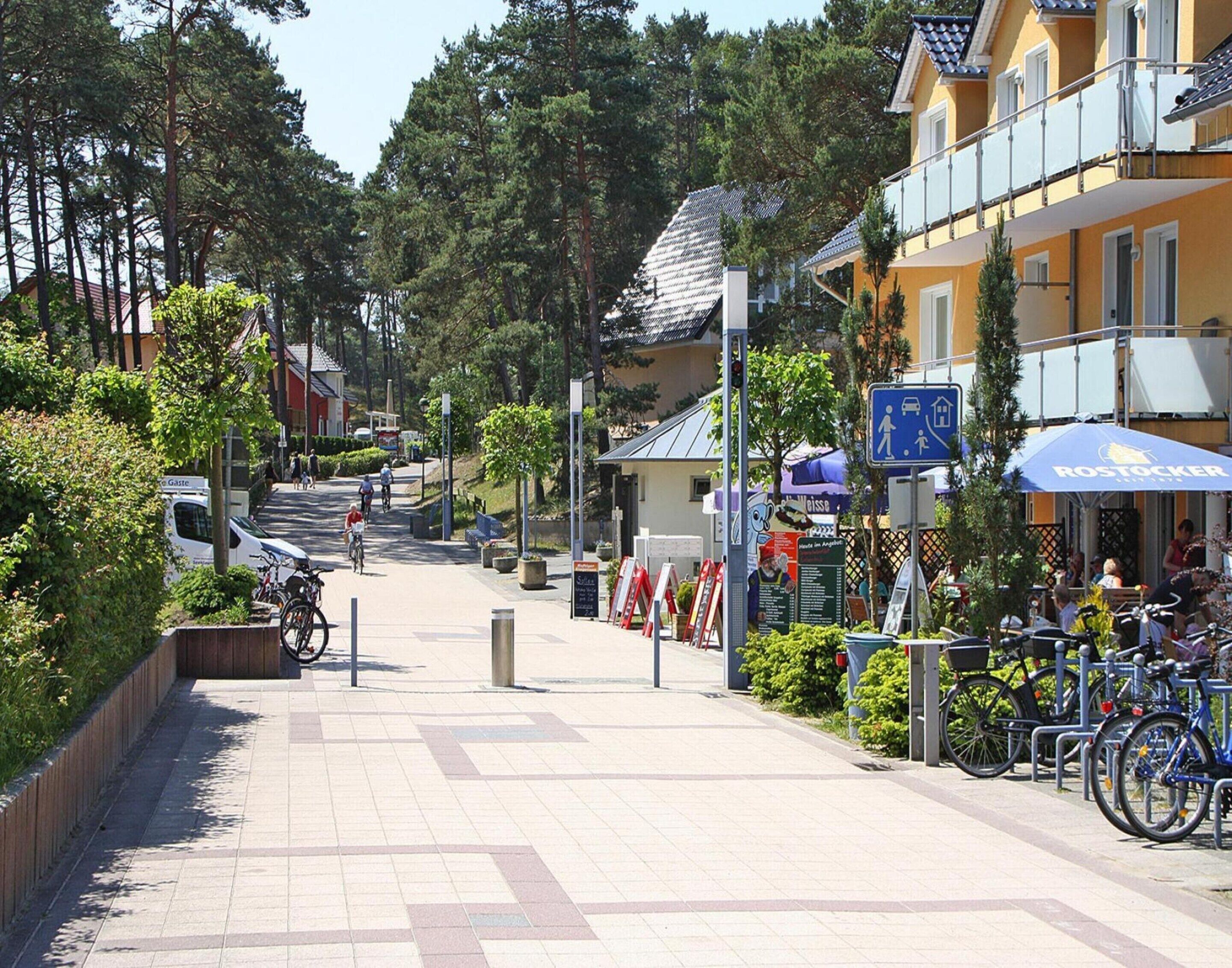 En asfalterad gångv äg med cyklar parkerade på höger sida, en blå skylt med en symbol för fotgängare och cyklister, och en byggnad med en gul fasad på höger sida.