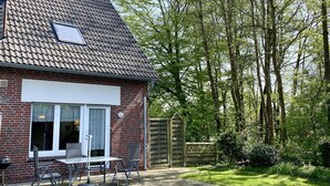 Une maison en briques avec un toit en tuiles, une porte vitrée et une terrasse avec une table et des chaises.