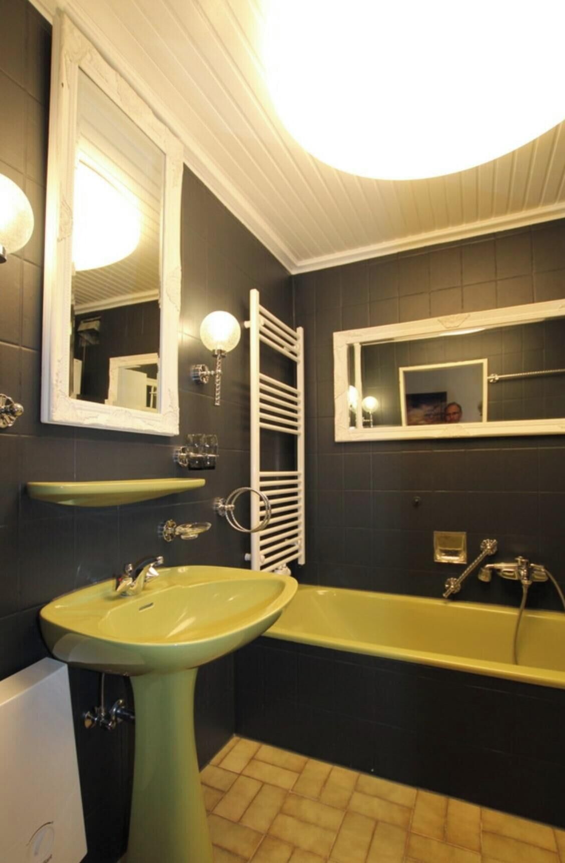 Une salle de bain avec un lavabo sur colonne, une baignoire et deux miroirs.