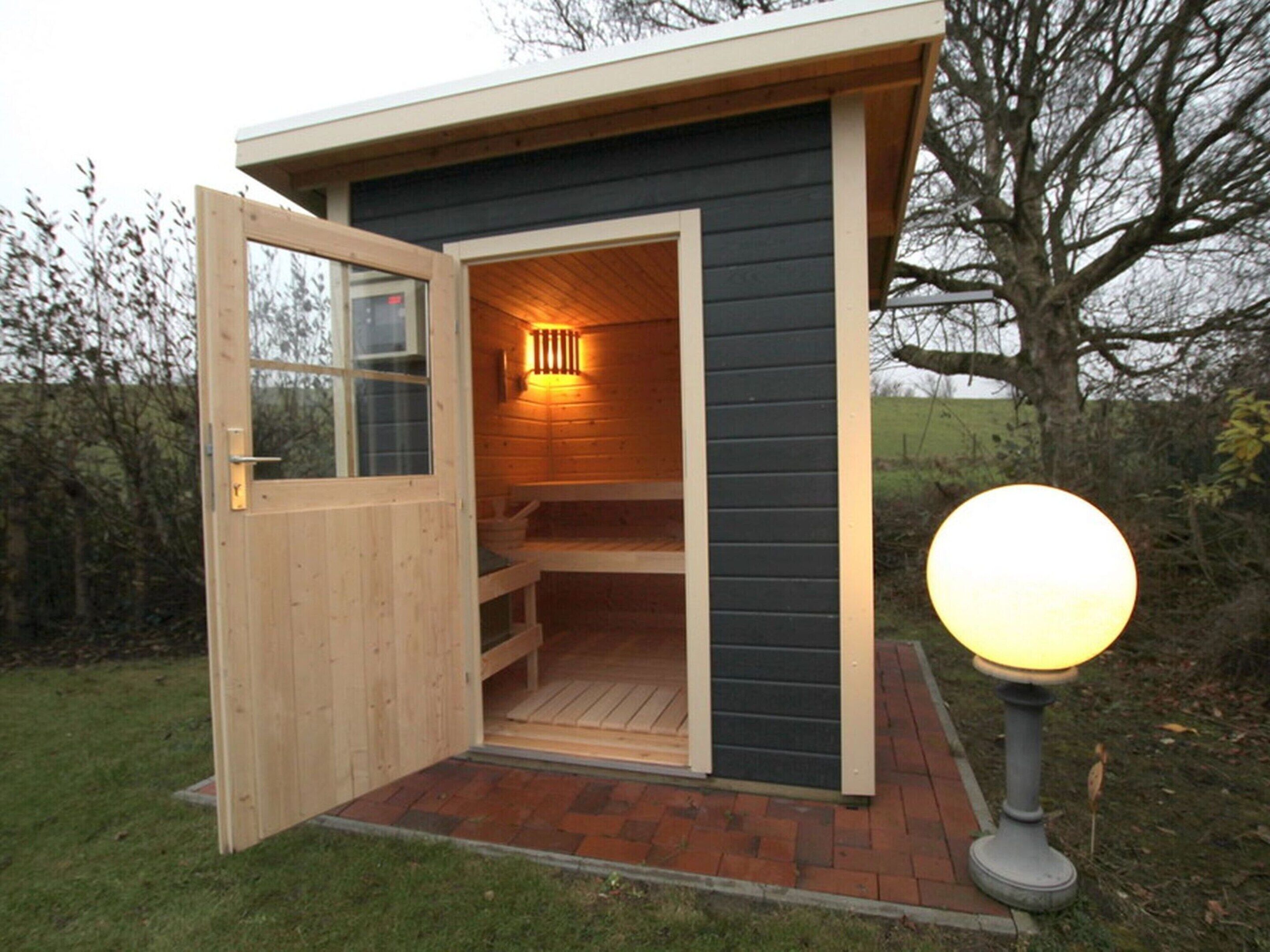 Une petite cabane en bois, dont la porte est ouverte, laissant apercevoir un banc à l’intérieur.